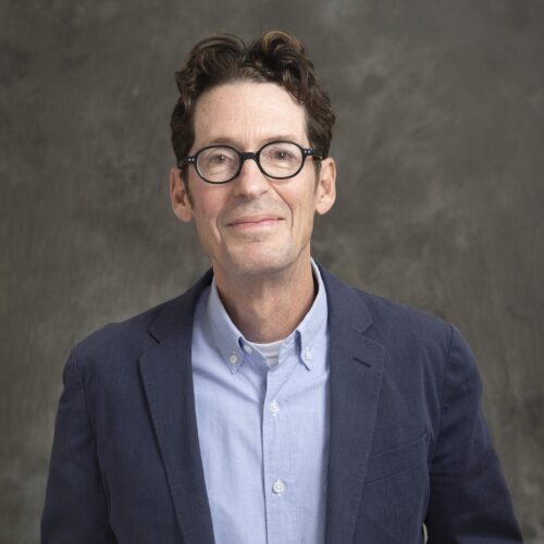 Professional headshot of a Knapp in a navy blazer and light blue shirt, smiling, against a gray background.