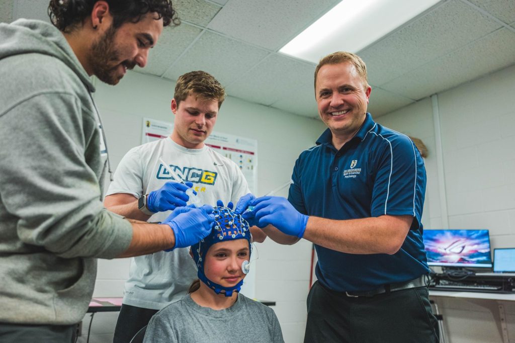 Drolette and two students place an electrode cap on a child