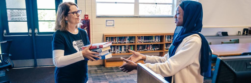 UNCG alumna hands a student a book to catalogue.