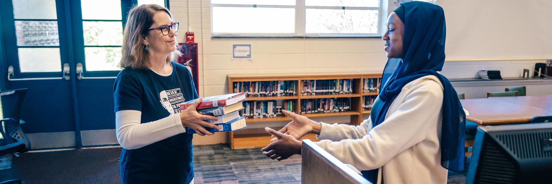 UNCG alumna hands a student a book to catalogue.
