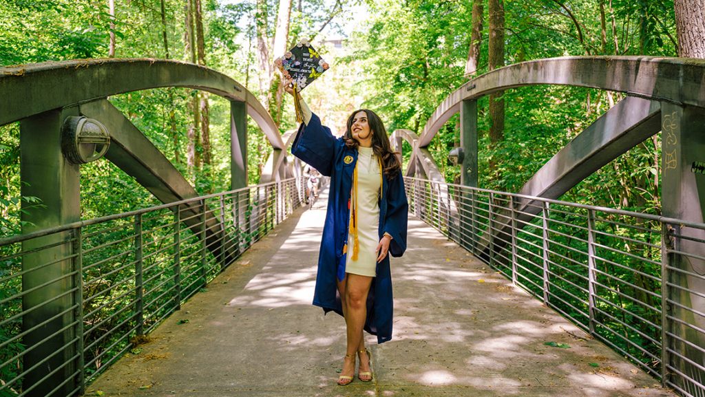 Graduate lifts her decorated cap and looks up on the bridge across Peabody creek.