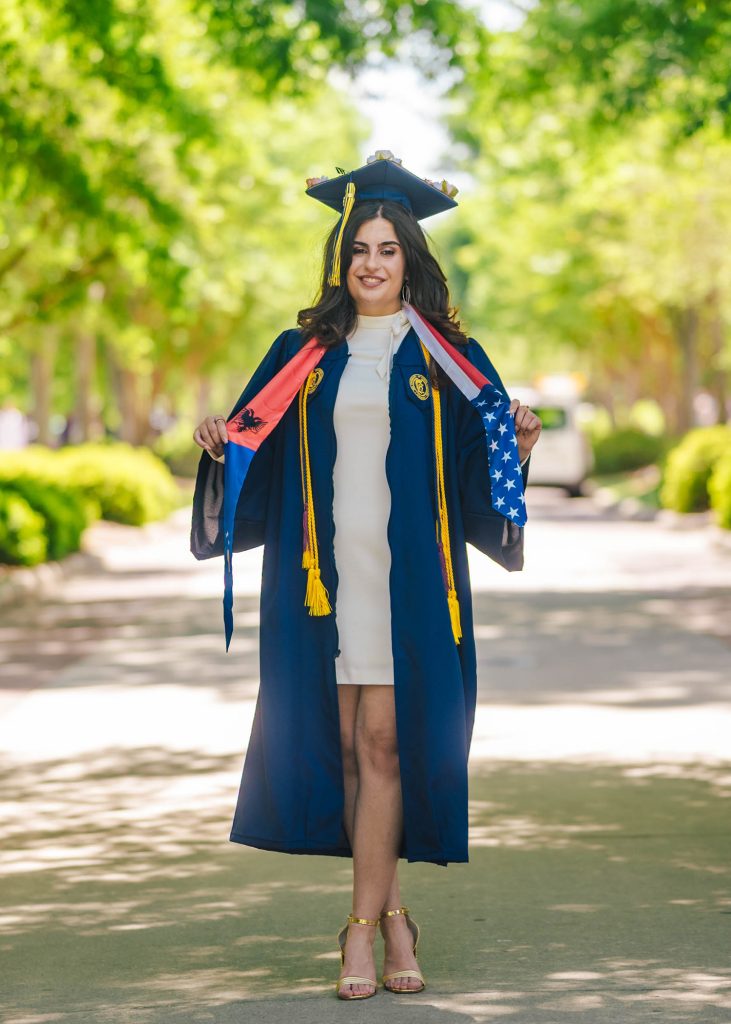 UNCG graduate poses on College Ave displaying her Albanian American sash.