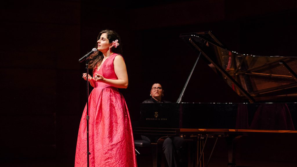 Singer on stage with a pianist on a baby grand in the background.