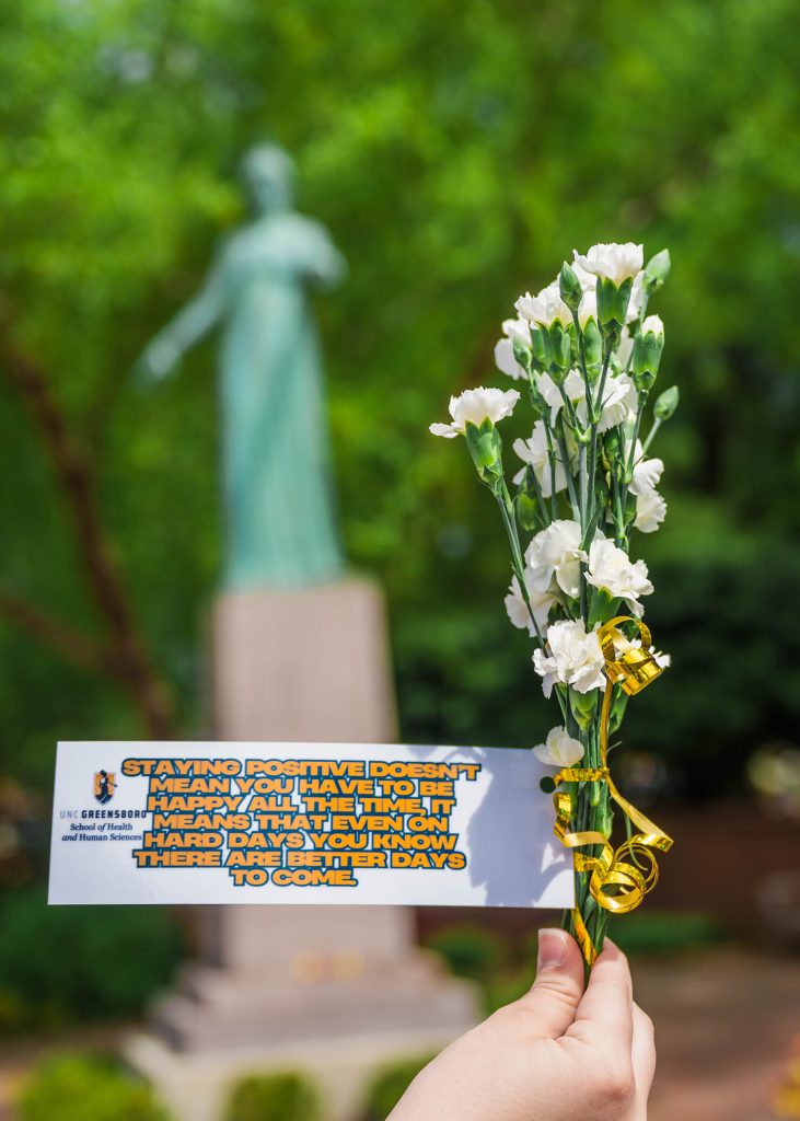 A hand holds flowers with a note about mental health and the minerva statue in the background.