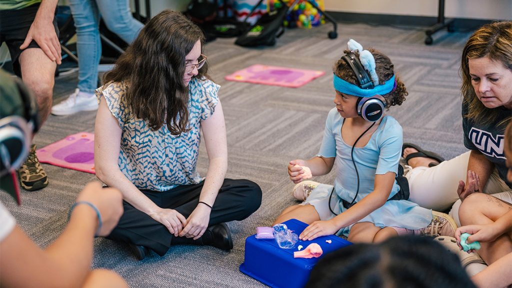 A girl with headphones talks to a UNCG student.