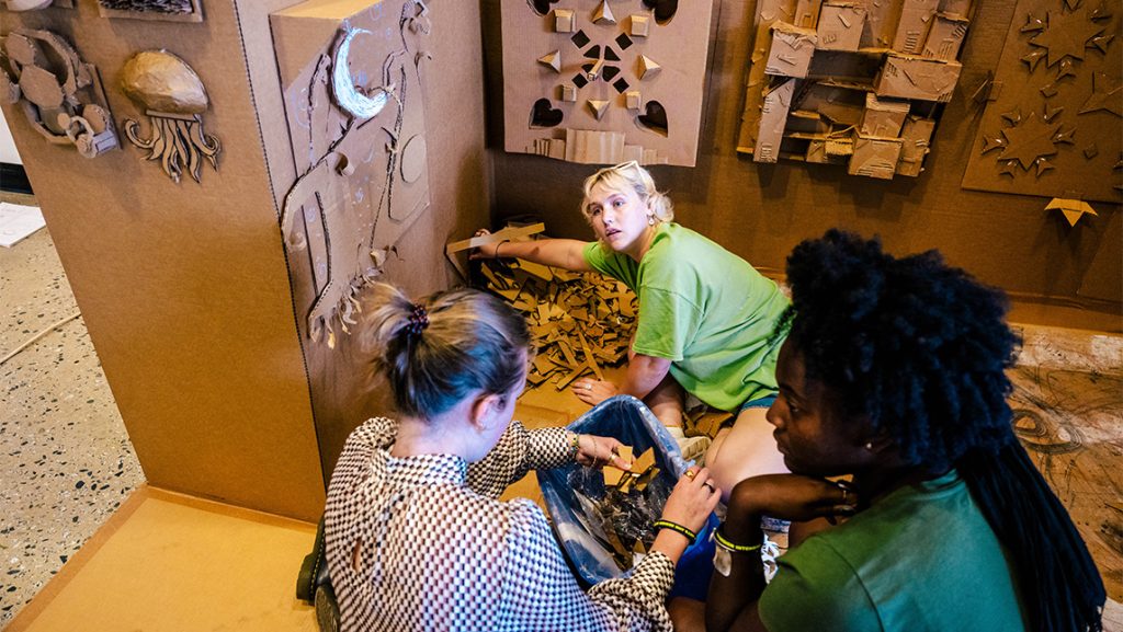 Children work on cardboard artwork.