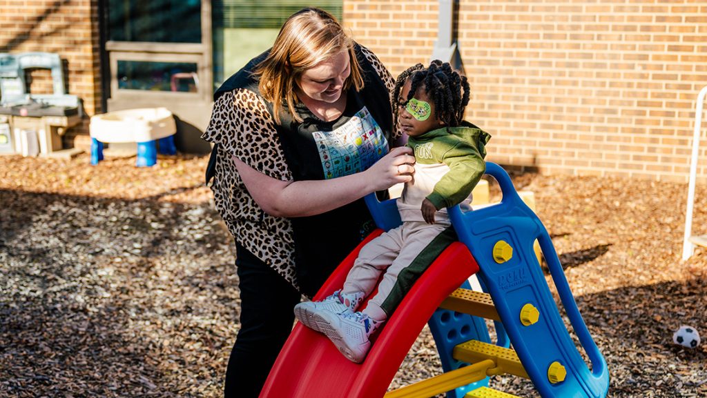 SLP Roslyn Reynolds helps a toddler down the slide.