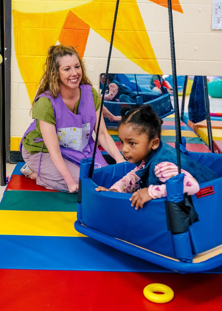 SLP Sarah Cunningham pushes a girl on an indoor swing.