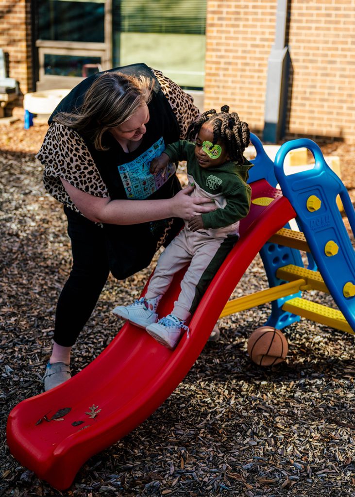 SLP Roslyn Reynolds helps a toddler down the slide.
