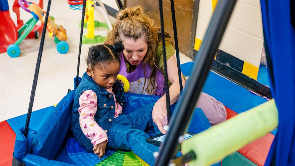 SLP Sarah Cunningham pushes a girl on an indoor swing.