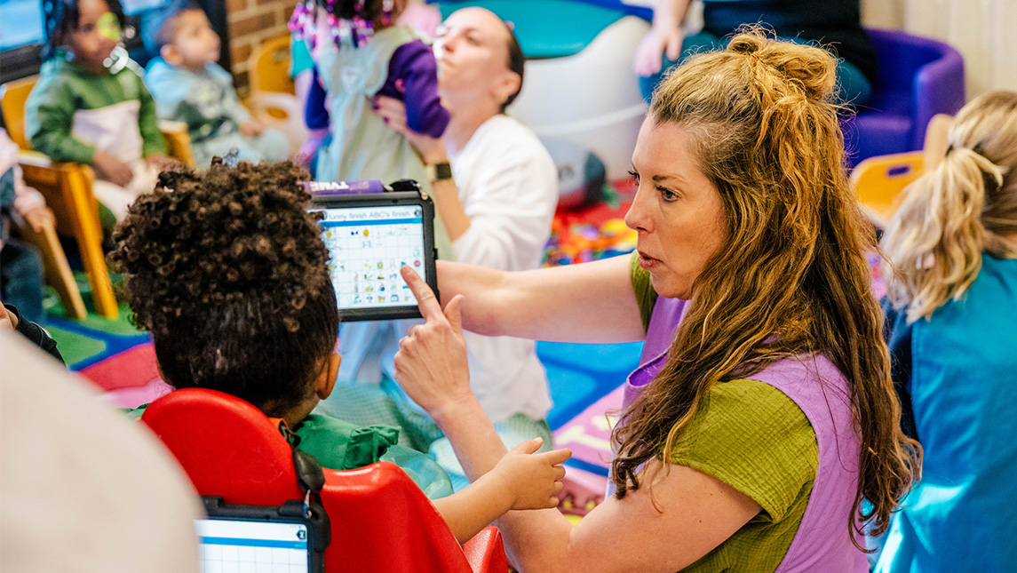SLP Sarah Cunningham points to pictures on a tablet for a child.