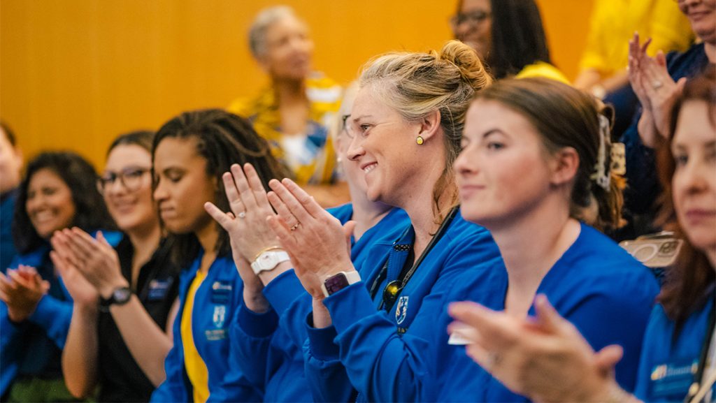 UNCG nursing students wearing scrubs applaud.
