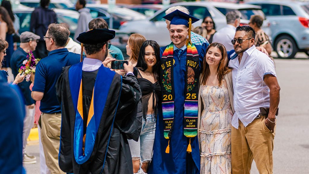 A UNCG professor takes a photo of a graduating student with his family.