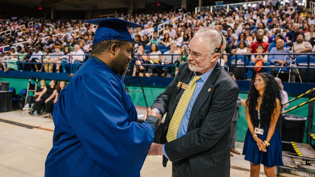A UNCG grad shakes hands with ITS staffer Moreland Smith at Commencement.
