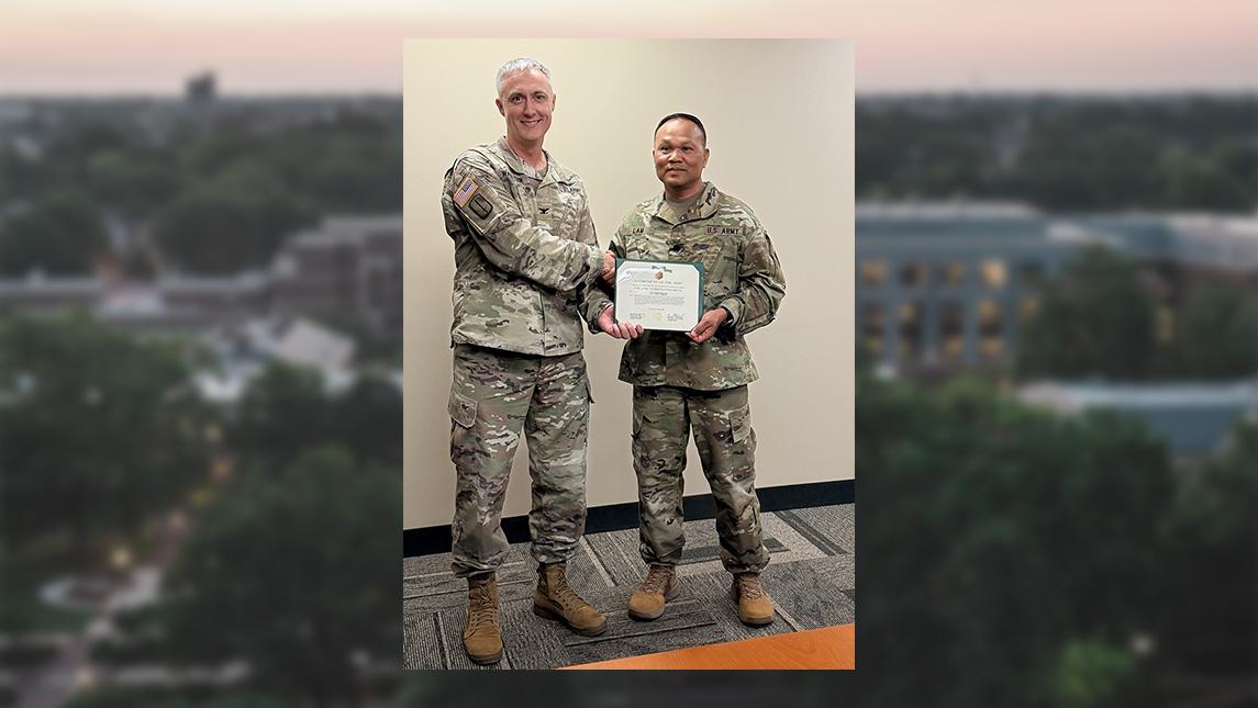Maj. SaQuang Lam wears Army fatigues while holding a certificate.