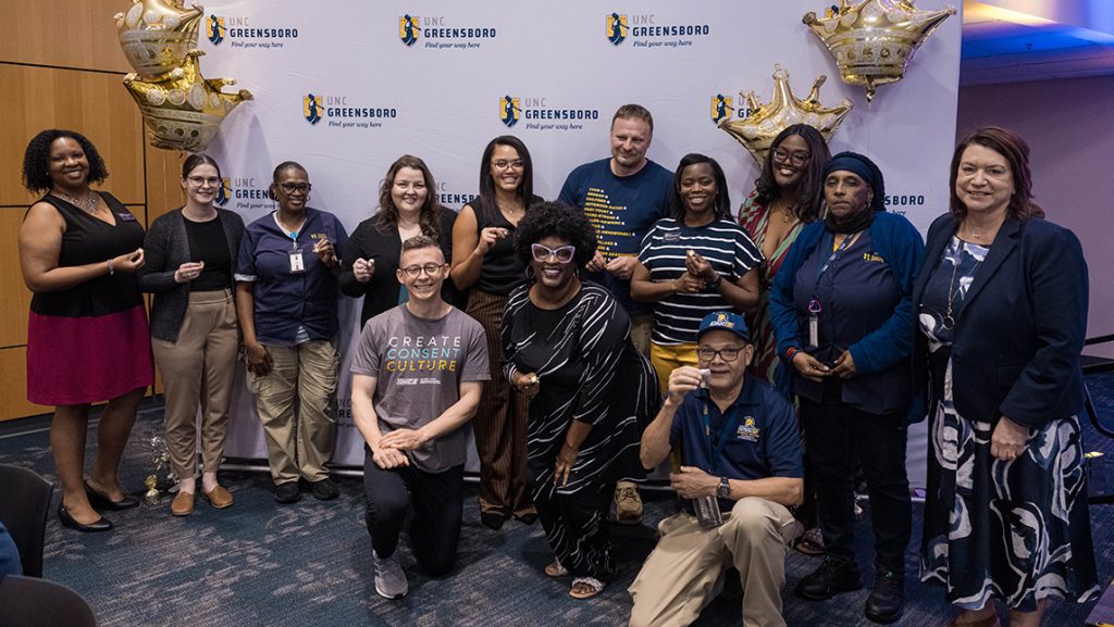 Student Affairs staff take a group photo in front of a UNCG backdrop.