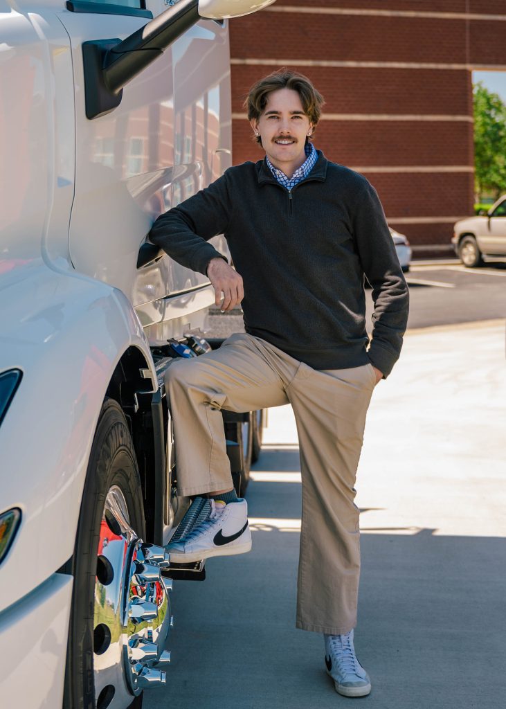 Student stands posed against a transfer truck.