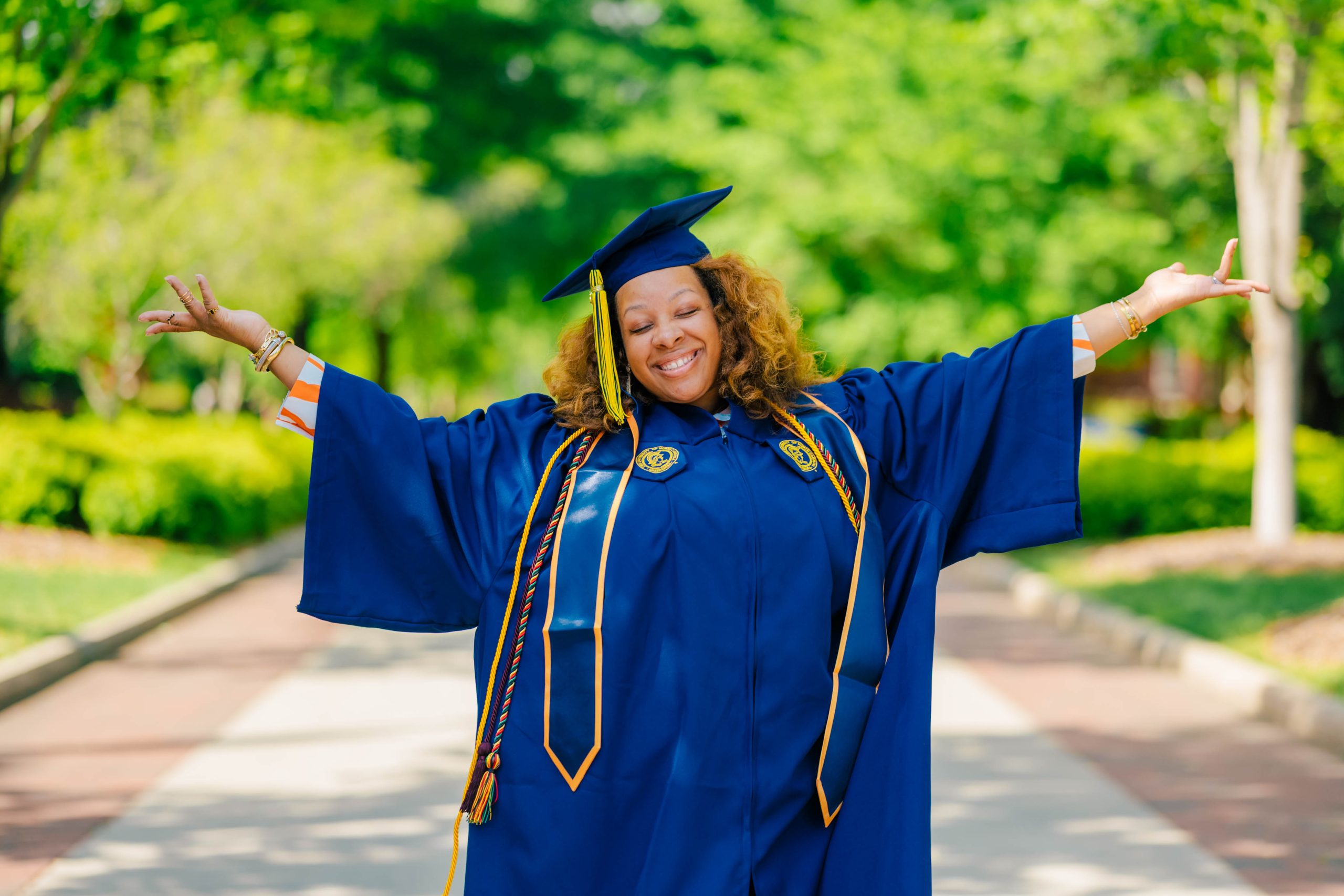 Naima Blakely holds up her arms while wearing her cap and gown.