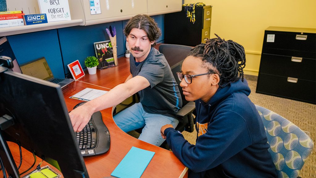 A UNCG advisor points to his computer while a student watches.