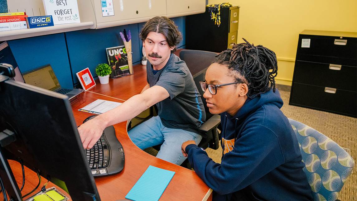 A UNCG advisor points to his computer while a student watches.