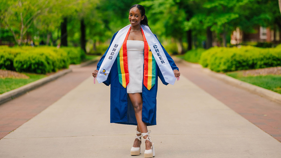 UNCG grad Samantha Flynn wearing her cap and gown and stoles.