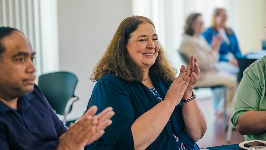 Nancy Brown claps while sitting at a table.