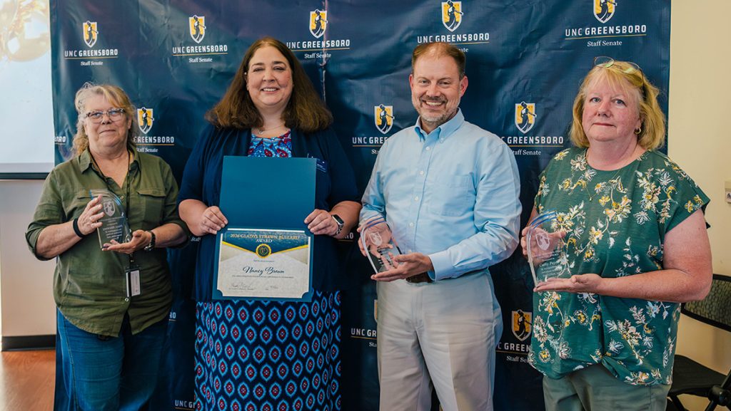 Four people hold up awards.