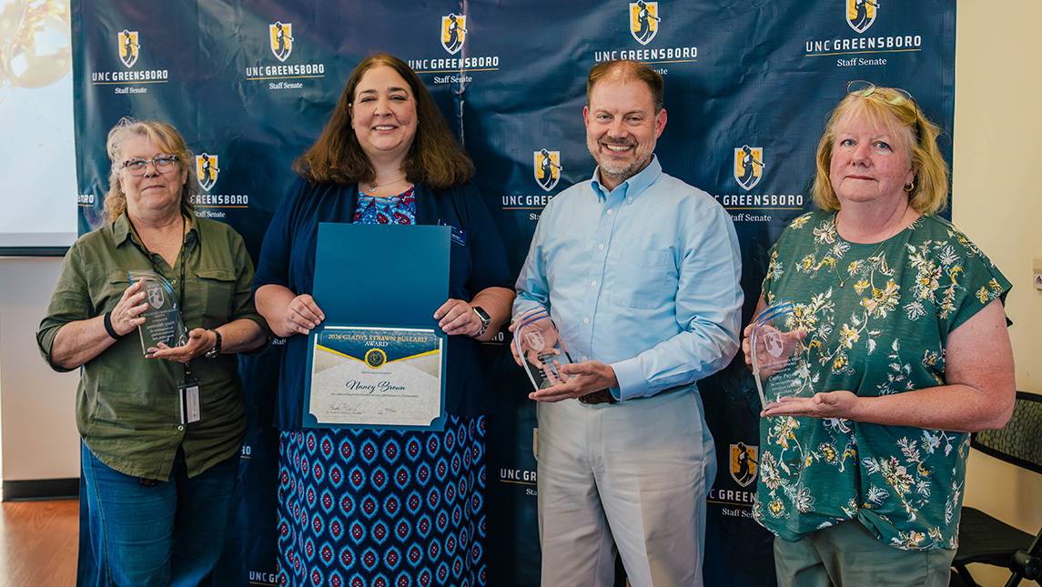 Four people hold up awards.