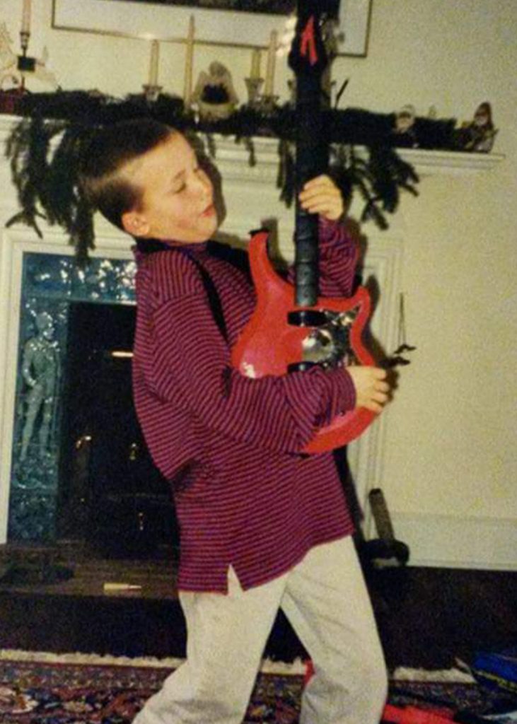 Young kid with an electric guitar plays in a living room decorated for Christmas.
