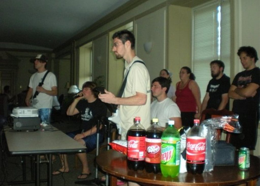 Students in a dormitory common room listen to guitarists and drummer play.