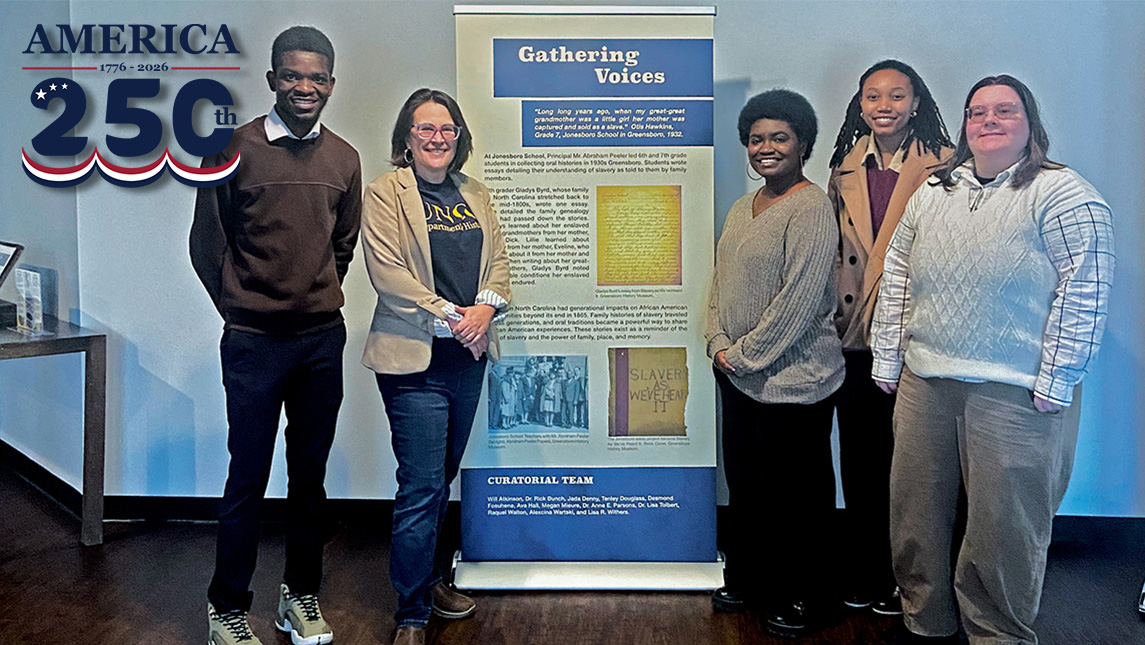 UNCG students and Dr. Anne Parsons stand next to their exhibit banner.