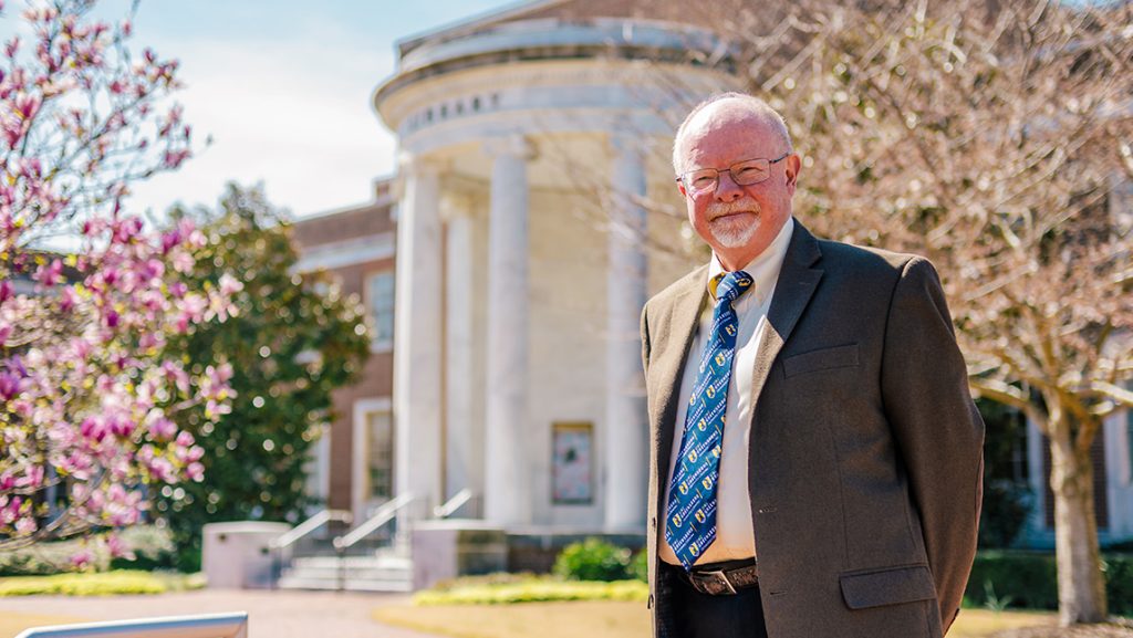 Dean Michael Crumpton wearing a suit and tie standing outside the UNCG library.