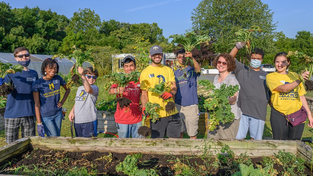 UNCG students hold up vegetables from a garden.