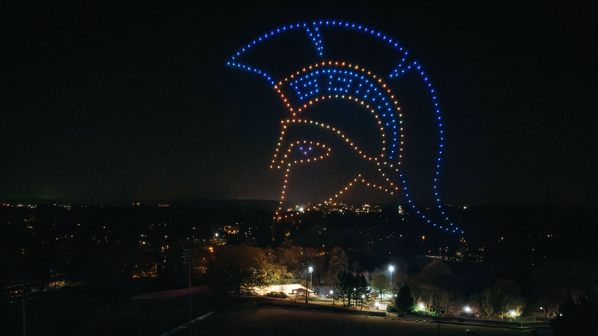 A drone show in the air where the drones have drawn out the Spartan helmet.