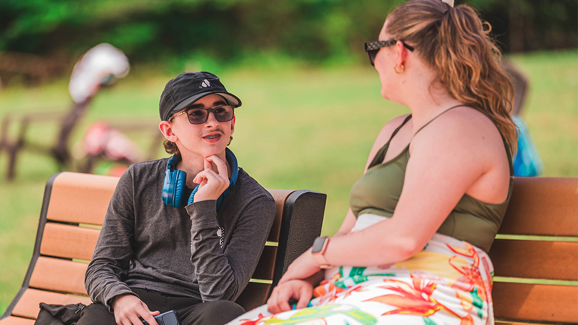 Two people sit and talk on a park bench.