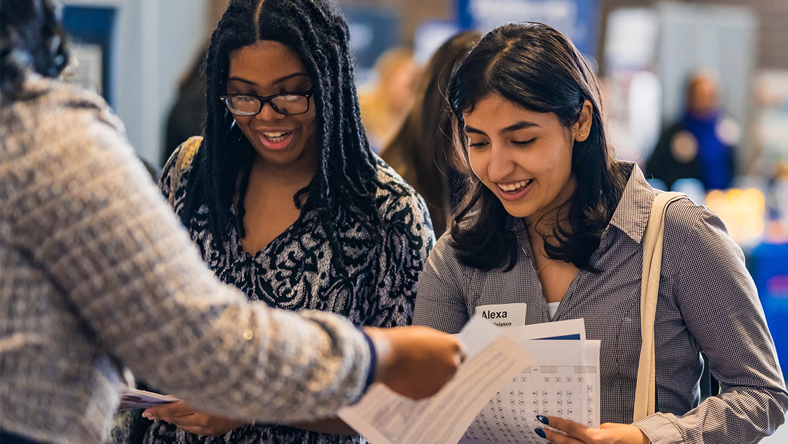 Two UNCG students share resumes with a job recruiter.