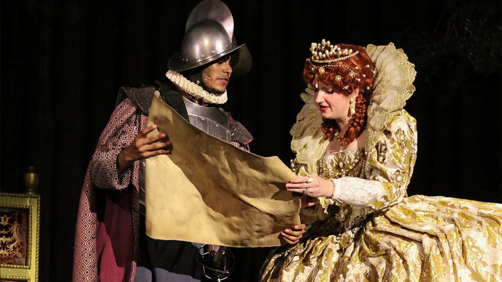 Actor Patrick Mullen dressed as a soldier holding a scroll for an actress dressed as Queen Elizabeth I.