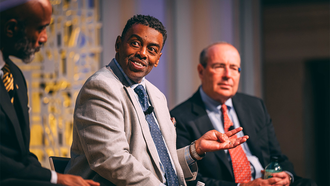 UNCG Chancellor Gilliam and two other men sit on a stage talking.