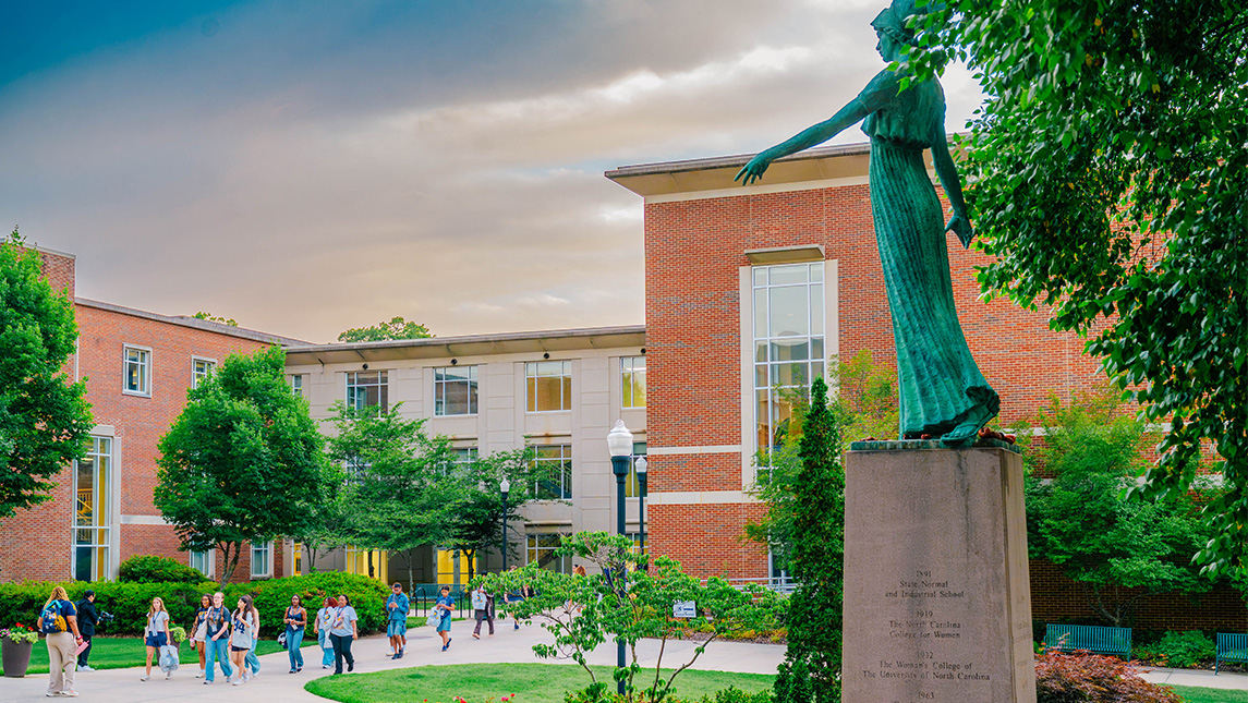 Students walk across a college campus and a statue of Minerva.
