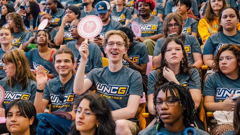 Students wearing matching UNCG t-shirts hold paddles that say "1G."