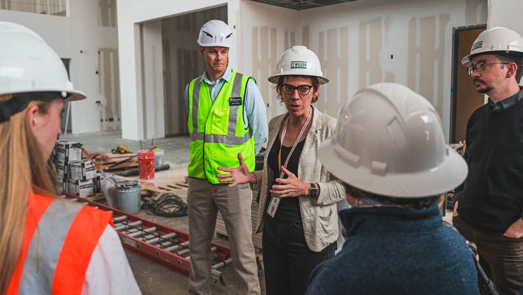Juliette Bianco talks to a group of people in the middle of a building under construction.