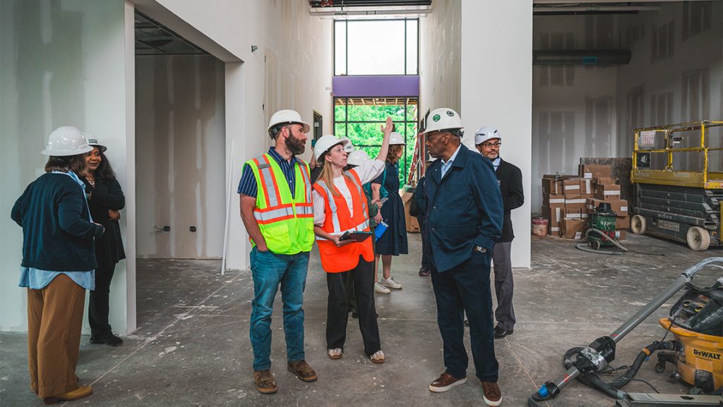 A group of people waring hard hats look around a building under construction.