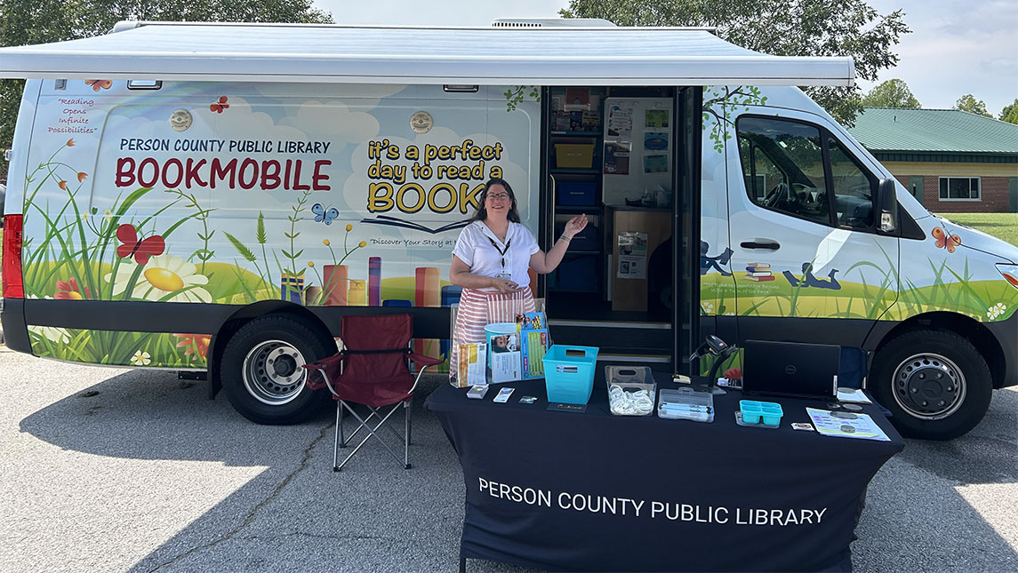a lady stands in front of a book mobile