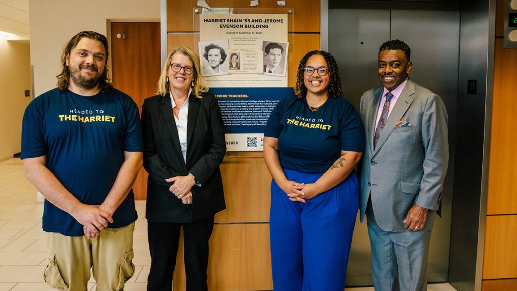 UNCG Chancellor Gilliam stands with three students next to a picture of Harriet Shain.