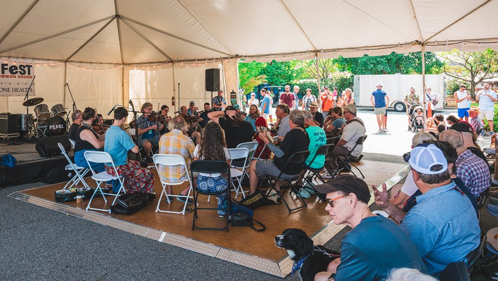 A group of people play musical instruments beneath an outdoor tent.