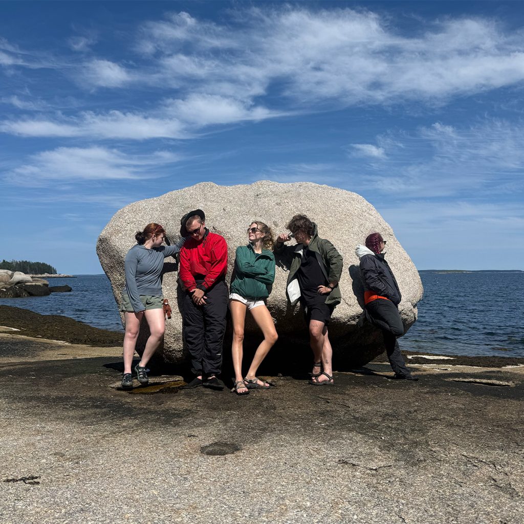 People strike poses next to a giant rock on a beach.