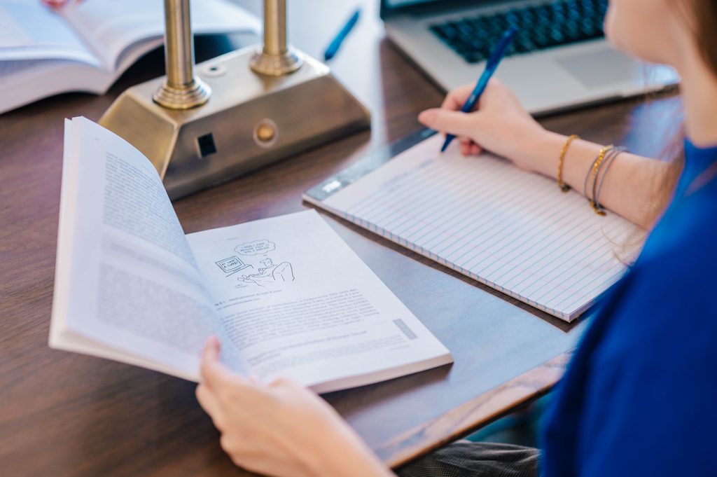 Open textbook, notebook, and laptop on a desk as a student takes notes during class preparation.