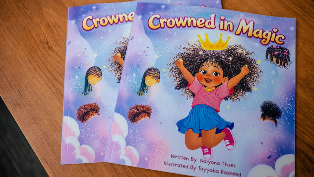 Two copies of Crowned in Magic, a children’s book by Naiyana Thues, displayed on a wooden table.