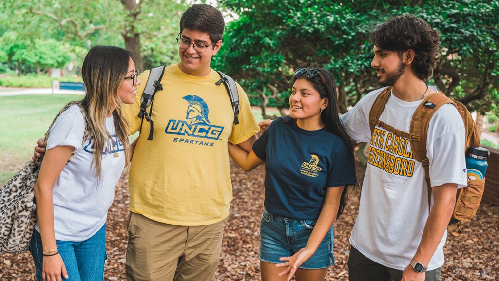 Group of students wearing UNCG shirts chat on campus.