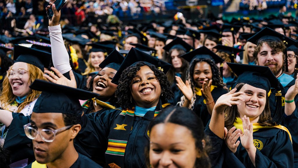 A group of college graduates smile in their cap and gowns.
